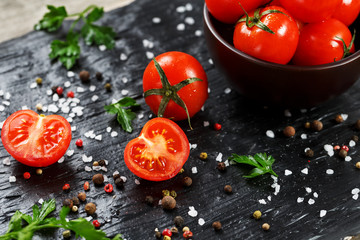 Fresh Sliced Cherry Tomatoes on a black background with spices coarse salt and herbs