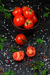 Fresh Sliced Cherry Tomatoes on a black background with spices coarse salt and herbs