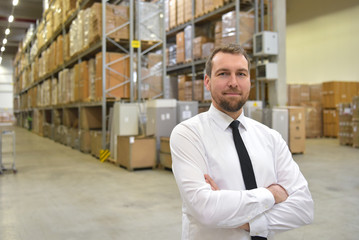 erfolgreicher Geschäftsmann im Anzug in einem Warenlager einer Spedition // successful businessman in a suit in a warehouse of a forwarding agency