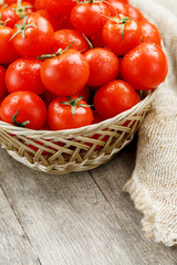 Small red tomatoes in a wicker basket on an old wooden table. Ripe and juicy cherry