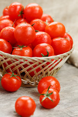 Small red tomatoes in a wicker basket on an old wooden table. Ripe and juicy cherry