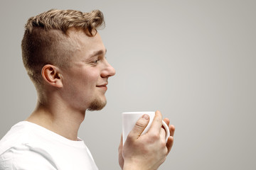 Taking a coffee break. Handsome young man holding coffee cup, smiling while standing against gray studio background