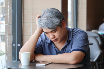 Stressed tired young Asian middle-aged man,old man take hand on head feeling depression and exhausted sitting by the window at coffee shop,grey hair man ,Family issues.