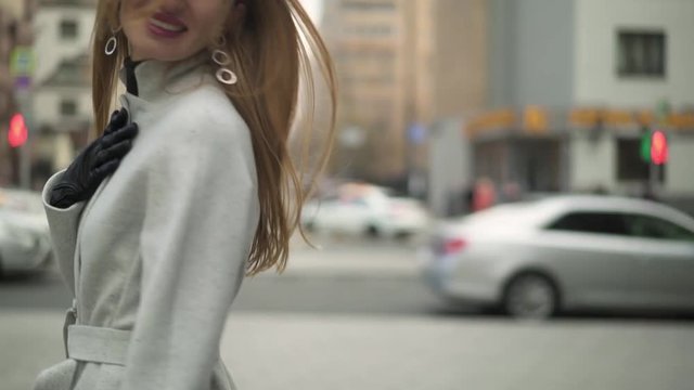 Slow motion attractive beautiful woman with long hair dressed in white coat and grey sweater coat walking turning around smiling and waving a hand gimbal shot