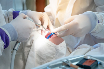 Female dentist and assistant hand using medicine syringe and other instruments for examining and curing patient teeth in dental clinic. Dental procedure and medical treatment.