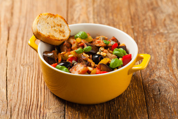Traditional Italian caponata, served with croutons in a yellow, sunny pot. Decorated with basil and pine nuts.
