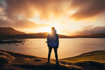 Man standing in blue jacket looking at spectacular sunset over frostadavatn lake in Landmannalaugar...