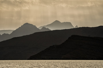 Silhouettes of mountains against the background of the sun. Ru'us al Jibal. Al Hajar Moutains. Musandam. Oman