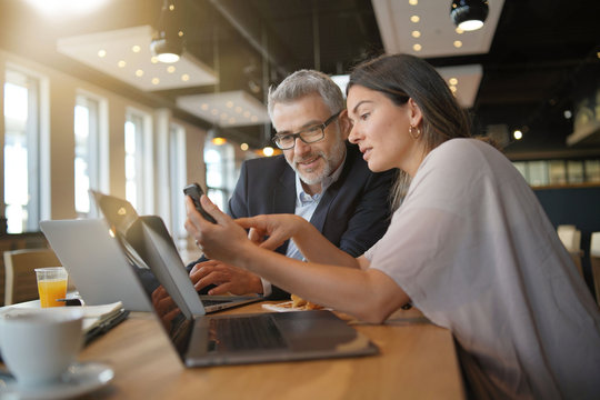 Young woman showing salesman stats on cellphone during informal meeting
