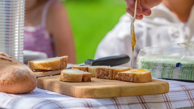 Someone is holding a spoo above a piece of bread and the honey is slowly running down on a piece of bread. Brealfast looks delicious.