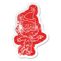 cartoon distressed sticker of a boy wearing sunglasses pointing wearing santa hat