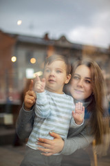 view through the panoramic window  to a happy couple of mom and child boy. family looks through the cafe windows, the mother shows a finger in the window and the son watches. selective focus