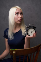 young blond girl with and glasses holding a clock. time management concept