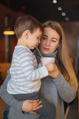 happy blonde mom and her little funny son rest in the cafe, drink tea and eat pies, have fun and have a nice family day together. selective focus, noise effect