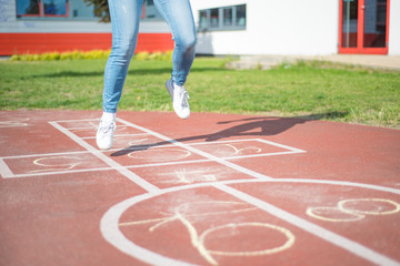 Girl jumping while playing Hopscotch at park. Close-up of little cute girls on children playground outdoors. Legs of kids jumps hopscotch on asphalt.