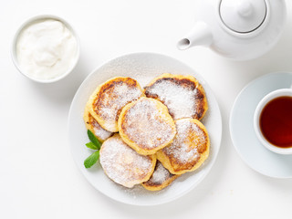 Cheesecake, curd fritters. Cottage cheese pancakes with powdered sugar. Sweet fried cheese pancakes on white plate on white background. Top view. Home tea party