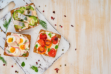Smorrebrod - traditional Danish sandwiches. Black rye bread with herring, egg, tomatoes, radish on white wooden table, top view