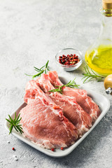 Raw meat, pork cutlets on a plate with rosemary, salt, pepper and olive oil. Selective focus, space for text.