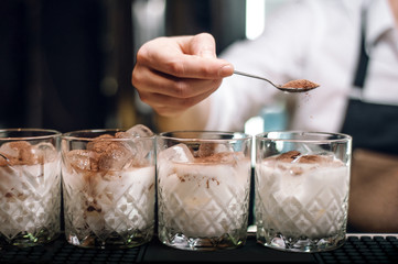 line of white russian cocktails at bar counter. barman sprinkles cocoa at cocktail.