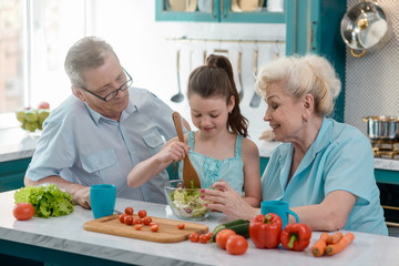 Child cooking salad for grandparents