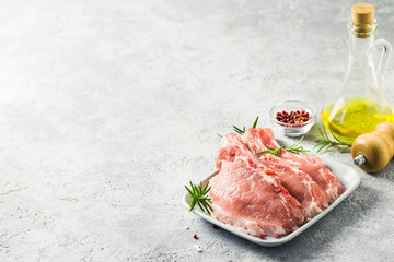 Raw meat, pork cutlets on a plate with rosemary, salt, pepper and olive oil. Selective focus, space for text.