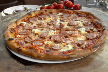 Pizza with tomato sauce, sausages, cheese and yellow cheese, olive oil, savory. On a wooden background with cherry tomatoes.