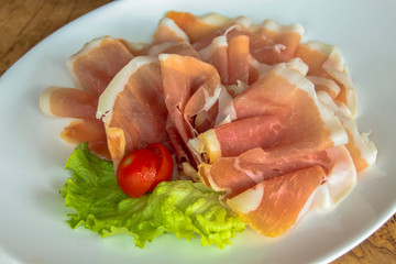 Cold appetizer - Prosciutto (ham), on a leaf of green salad, garnished with cherry tomato. Served...