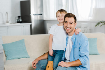 happy father and preschooler son hugging and looking at camera at home