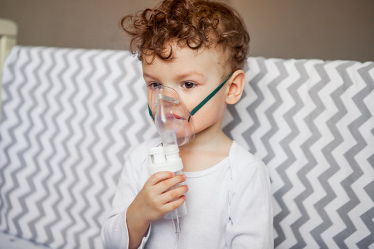 Inhalation Of The Respiratory Tract. Baby Sits With A Nebulizer In His Mouth, Inhaler, Treatment Of Bronchitis.