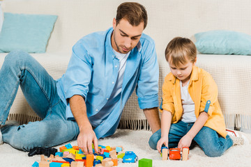 father and preschooler son playing with colorful building blocks and toy cars at home
