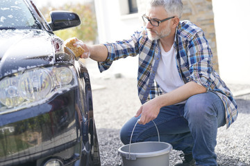 Mature man washing his car with soapy sponge in driveway