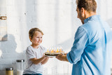 father giving birthday cake to adorable preschooler son in kitchen