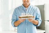 cropped view of smiling man holding birthday cake with burning candles at home in morning