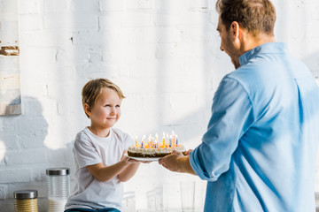 father giving birthday cake to adorable preschooler son in kitchen