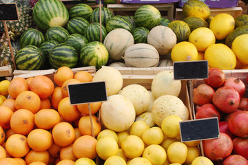 A counter on the farmers market shop with juicy fresh natural organic oranges, lemons, pomegranates, melons and watermelons and empty slate price tags for text and price.