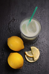 VASO DE ZUMO DE LIMÓN CON HIELO Y LIMONES SOBRE FONDO DE MADERA CON GOTAS DE AGUA