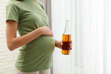 Pregnant woman with bottle of beer indoors, closeup. Alcohol abuse during pregnancy