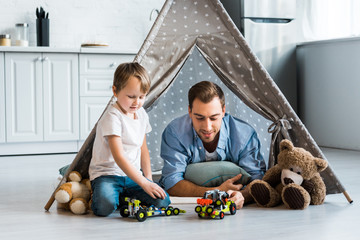 father and preschooler son playing with toy cars and teddy bears under wigwam at home © LIGHTFIELD STUDIOS