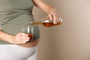 Fototapeta premium Pregnant woman pouring whiskey into glass on color background, space for text. Alcohol addiction