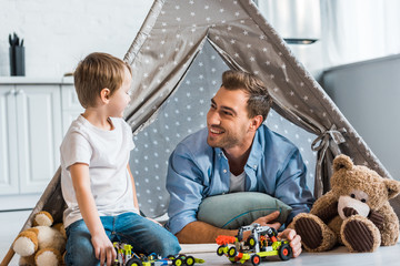 smiling father and preschooler son playing with toy cars and teddy bears under wigwam at home © LIGHTFIELD STUDIOS