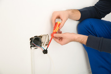 Electrician with screwdriver repairing power socket indoors, closeup