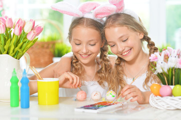 Obraz na płótnie Canvas Portrait of cute twins wearing rabbit ears decorating Easter eggs