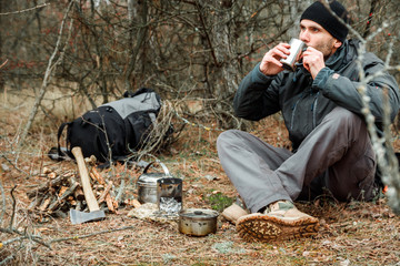 man relaxing in the forest camping, near the wood stove, utensils and axe with firewoods