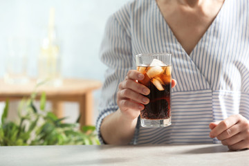 Woman with glass of cold cola at table indoors, closeup. Space for text