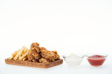 crispy chicken nuggets near french fries and glass bowls with ketchup and mayonnaise isolated on white