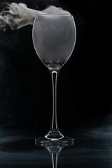 Closeup glass with white fog at dark background. Chemical reaction of dry ice with water.