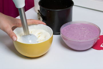 Blueberry cheesecake. A woman will mix a blender sour cream in cottage cheese jelly. Ingredients for cooking are located on the surface of the table.