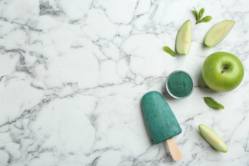 Flat lay composition with delicious spirulina popsicle on marble table. Space for text