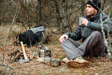 Fototapeta na wymiar man relaxing in the forest camping, near the wood stove, utensils and axe with firewoods