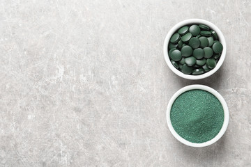 Bowls of spirulina pills and powder on color background, top view. Space for text